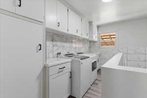 Laundry room featuring white cabinetry, marble-patterned tile backsplash and included washer and dryer.