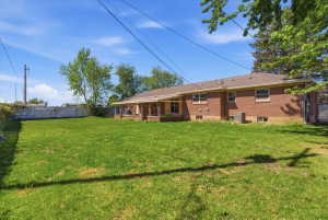 Large green lawn with mature trees featuring multiple windows and a covered patio area