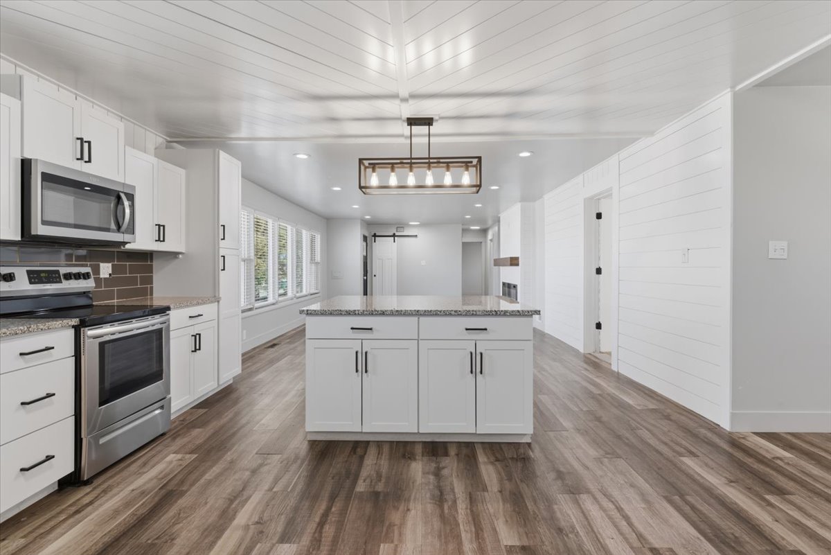 Kitchen with a large central island, white cabinetry, included stainless steel appliances, and granite countertops