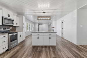 Kitchen with a large central island, white cabinetry, included stainless steel appliances, and granite countertops