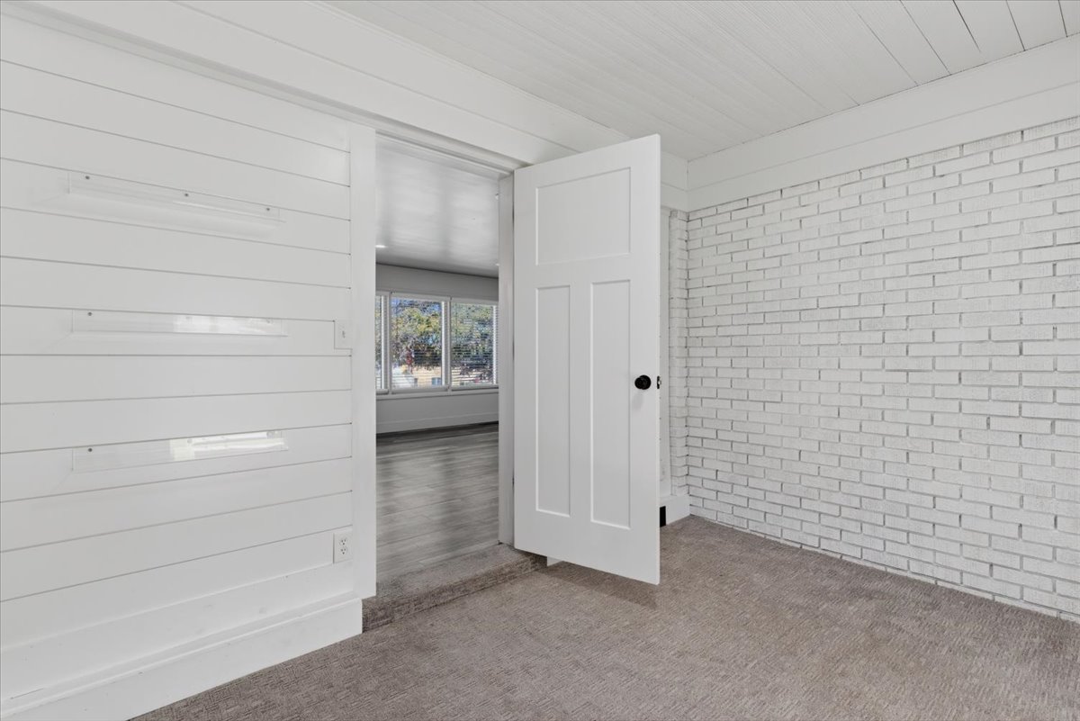 Bedroom featuring white shiplap walls, a white painted brick accent wall, and carpet flooring