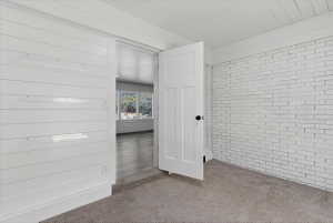 Bedroom featuring white shiplap walls, a white painted brick accent wall, and carpet flooring