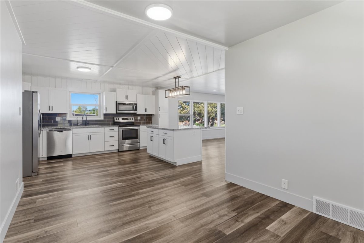 Kitchen featuring white cabinetry, included stainless steel appliances, a center island, vinyl flooring, and a dark tile backsplash