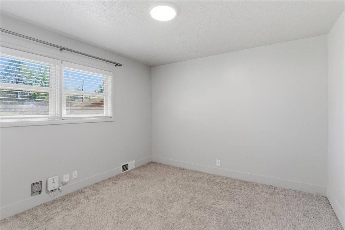 Bright bedroom featuring large windows with blinds, light gray walls, a flush-mount ceiling light, light-colored carpeting, and white baseboards