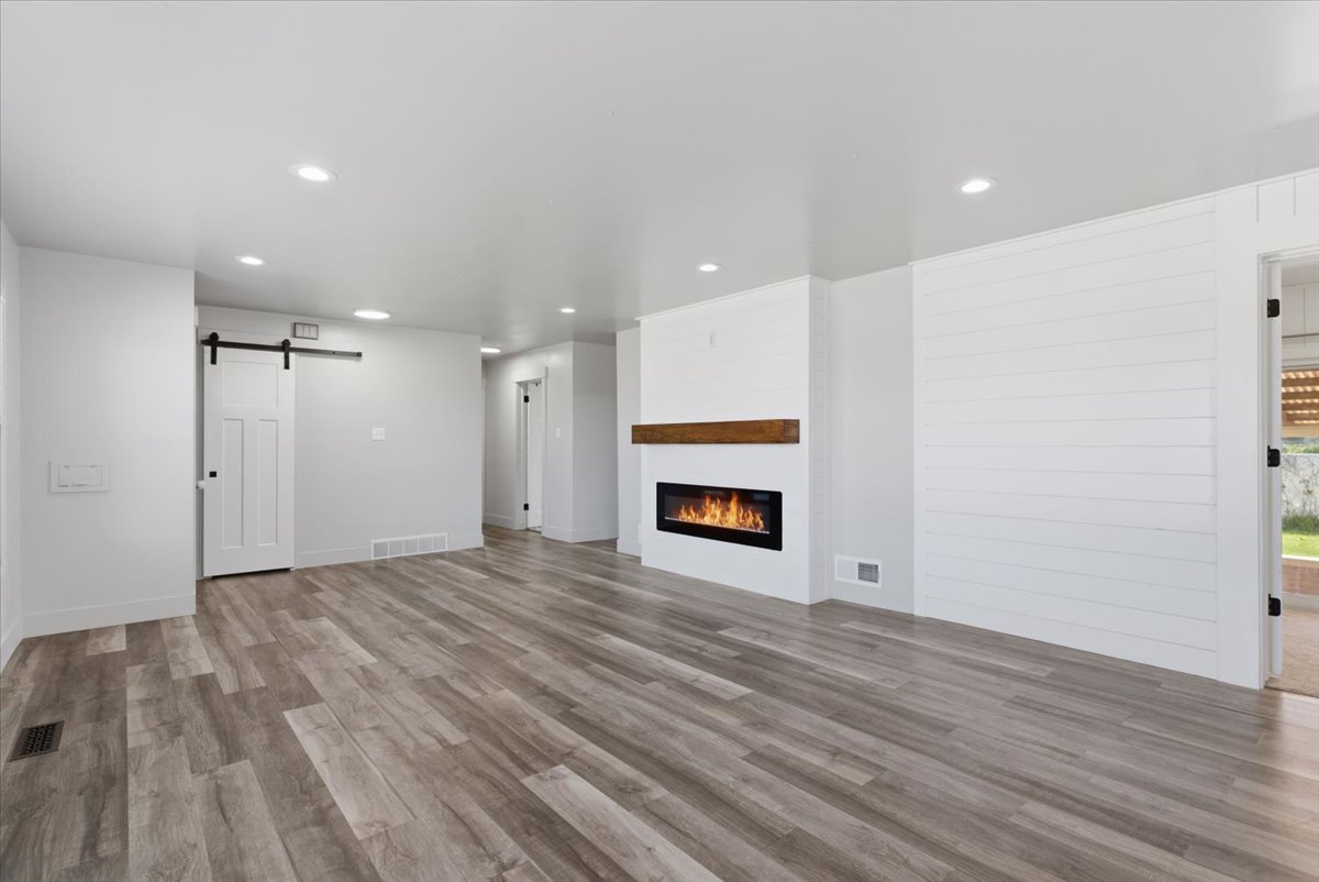 Spacious room featuring vinyl flooring, recessed lighting, and an electric fireplace with a wood mantle