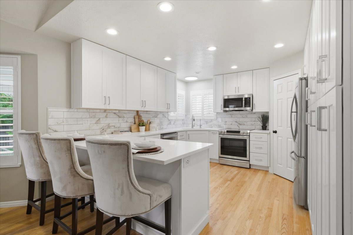 Contemporary kitchen featuring a breakfast bar island, white shaker cabinetry, stainless steel appliances, and wood-finish flooring