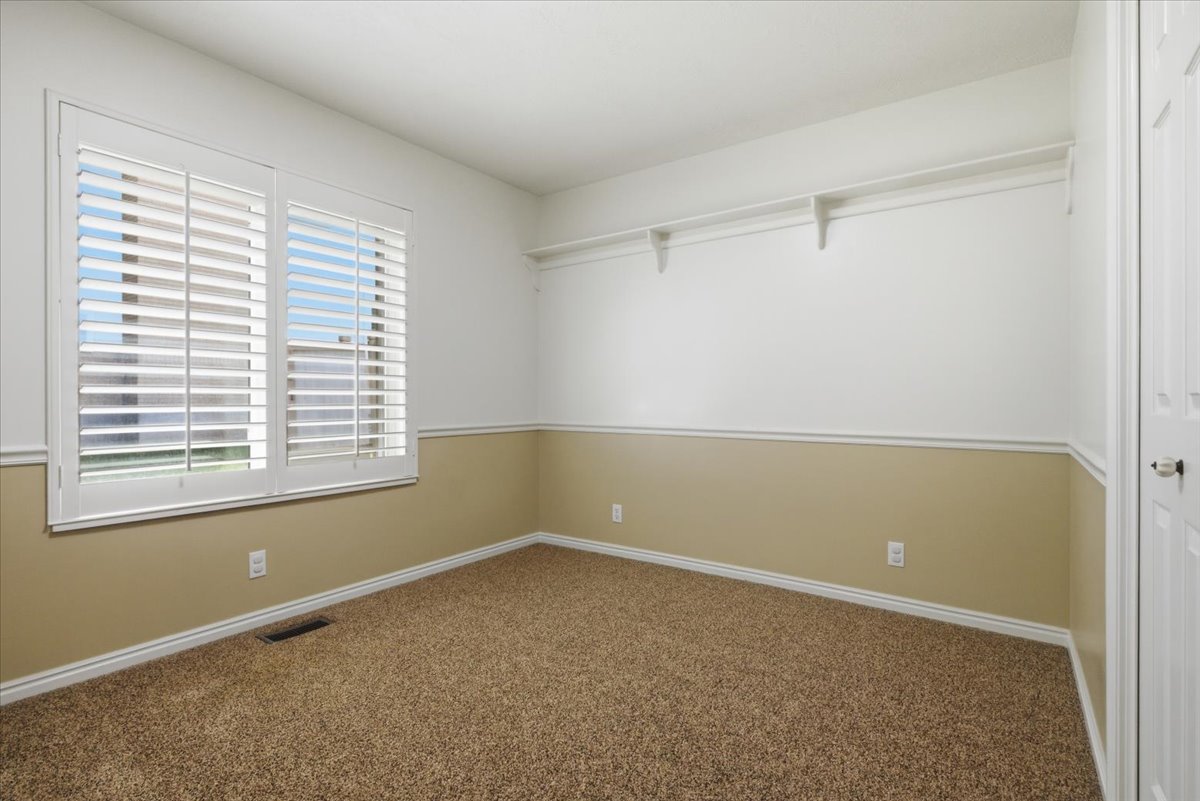 Carpeted room featuring a double window with plantation shutters, two-tone wall paint with wainscoting, and a built-in closet shelf