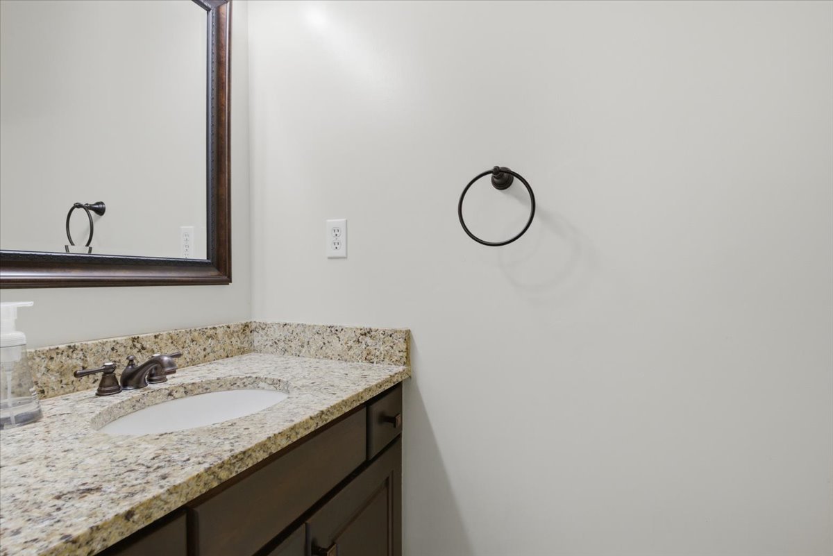 Bathroom vanity featuring a light-colored granite countertop, an undermount sink, and dark wood-finish cabinetry