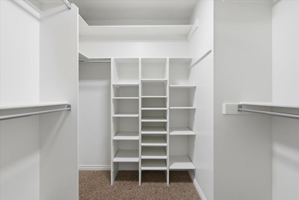 Spacious walk-in closet featuring built-in shelving units, multiple hanging rods, and light brown carpeting