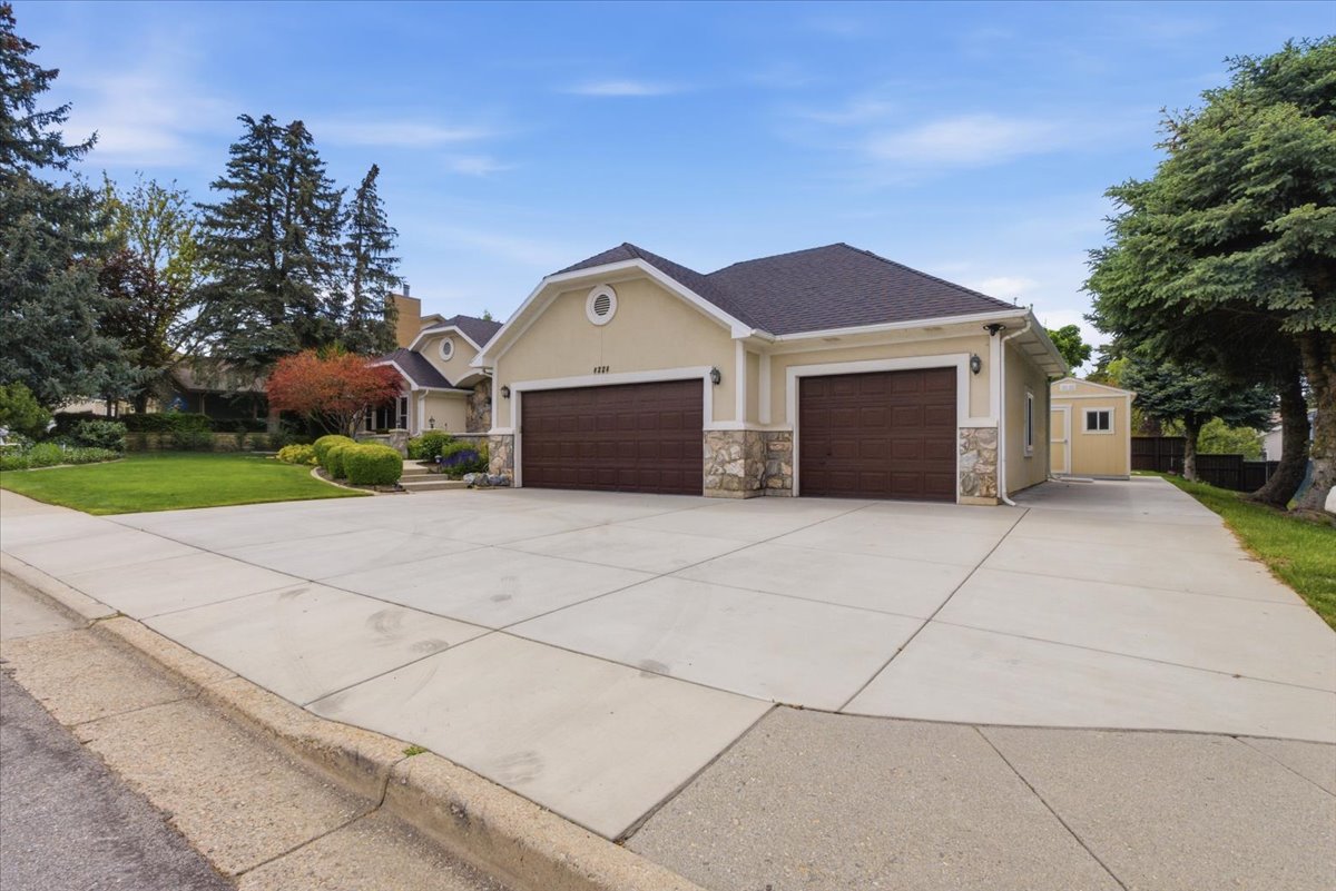 Exterior featuring a two-car garage with dark wood-finish doors, stone accents, stucco siding, and a gabled roofline