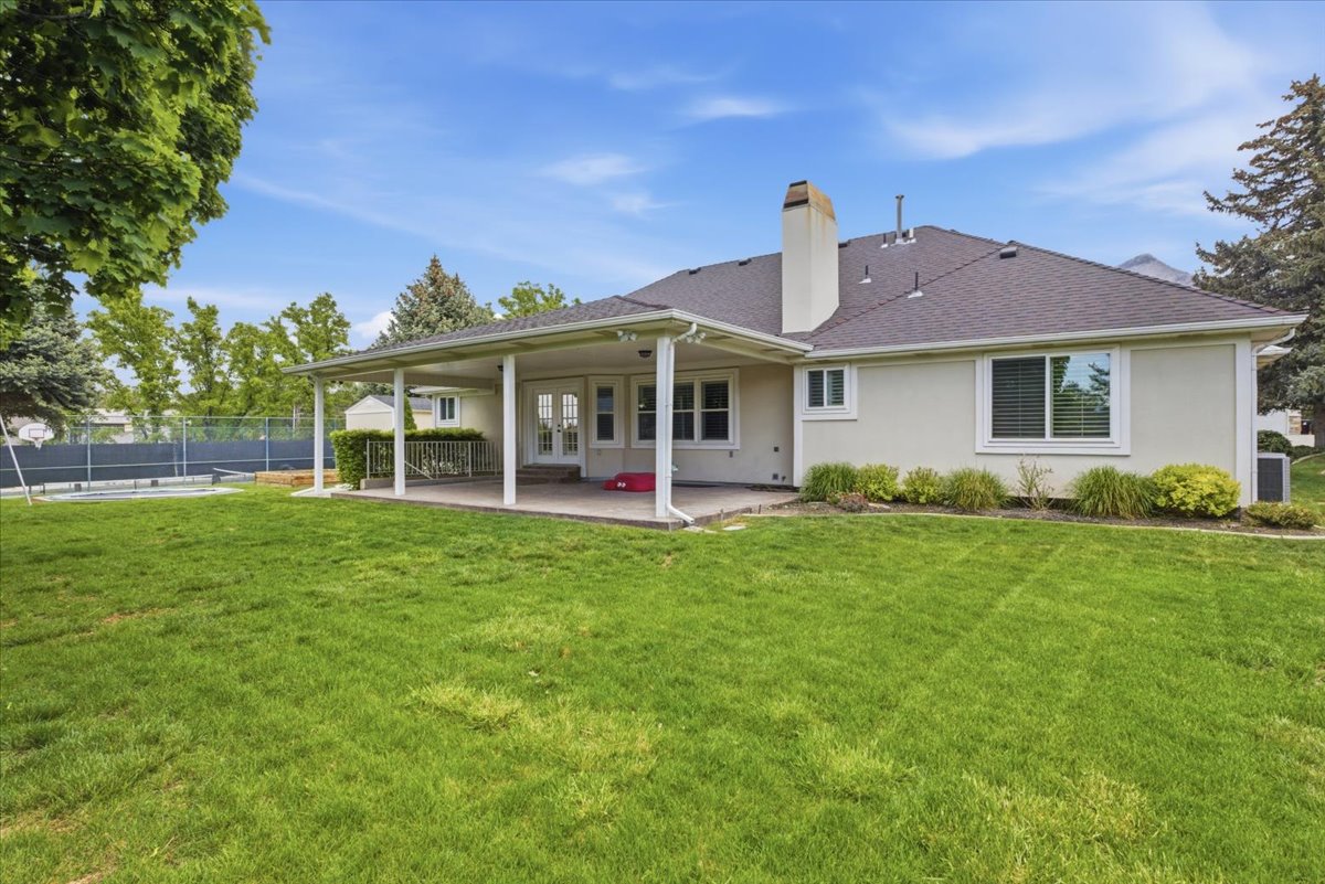 Expansive rear exterior featuring a covered patio, a broad lawn area, and mature perimeter trees
