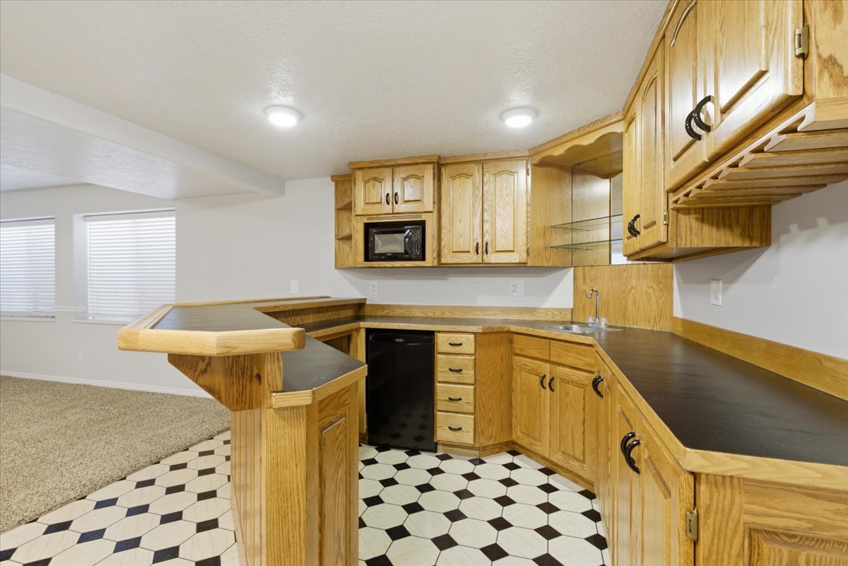Kitchenette featuring wood cabinetry, black countertops, integrated microwave, compact refrigerator, and a stainless steel sink