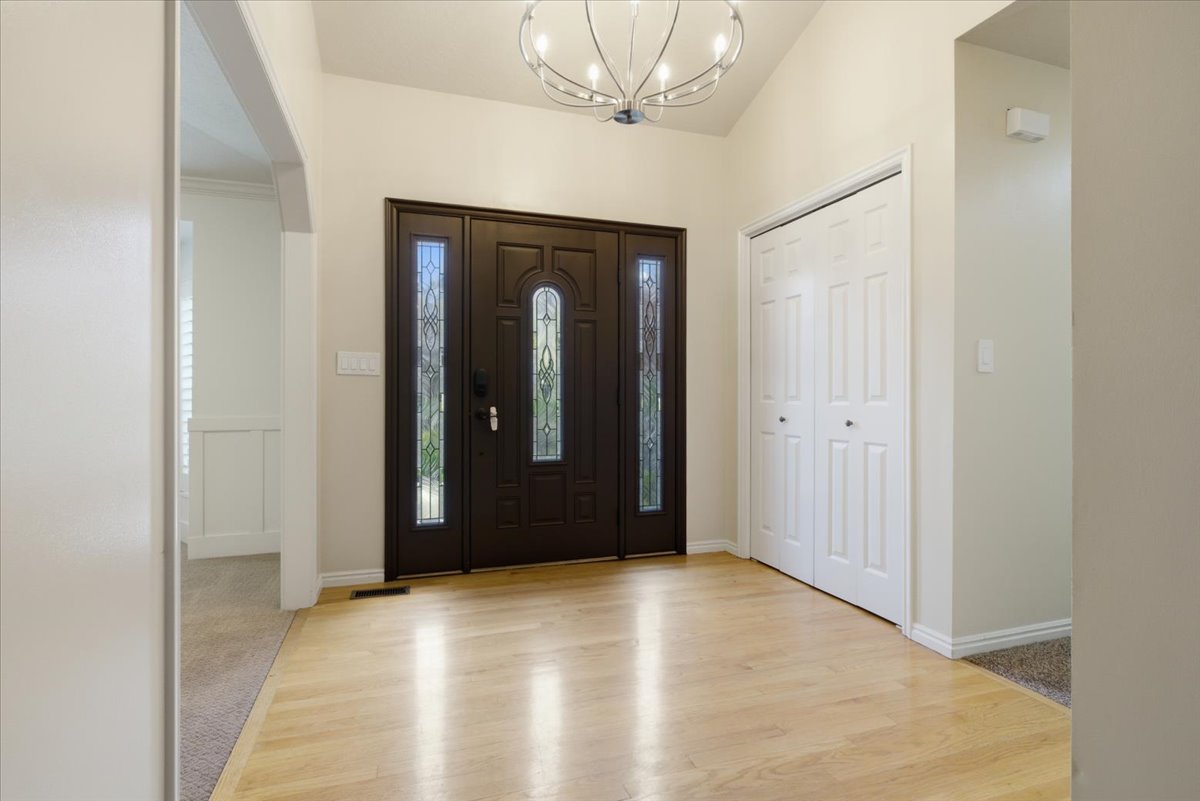 Entryway featuring a dark wood double door with decorative glass sidelights, a contemporary chandelier, light wood-finish flooring, and white bifold closet doors
