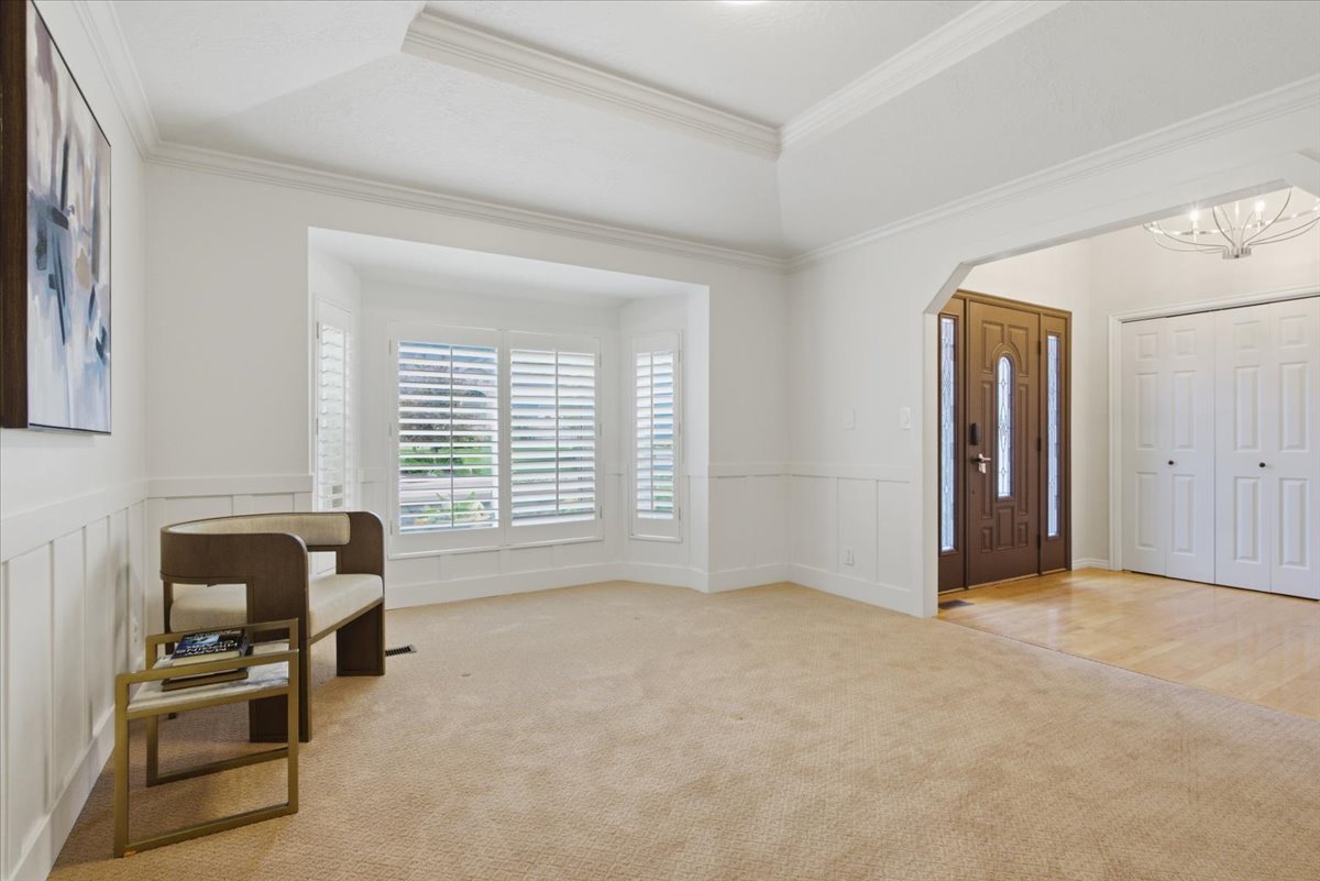 Bay window with plantation shutters, wainscoting, tray ceiling, arched entryway, and wood-finish flooring