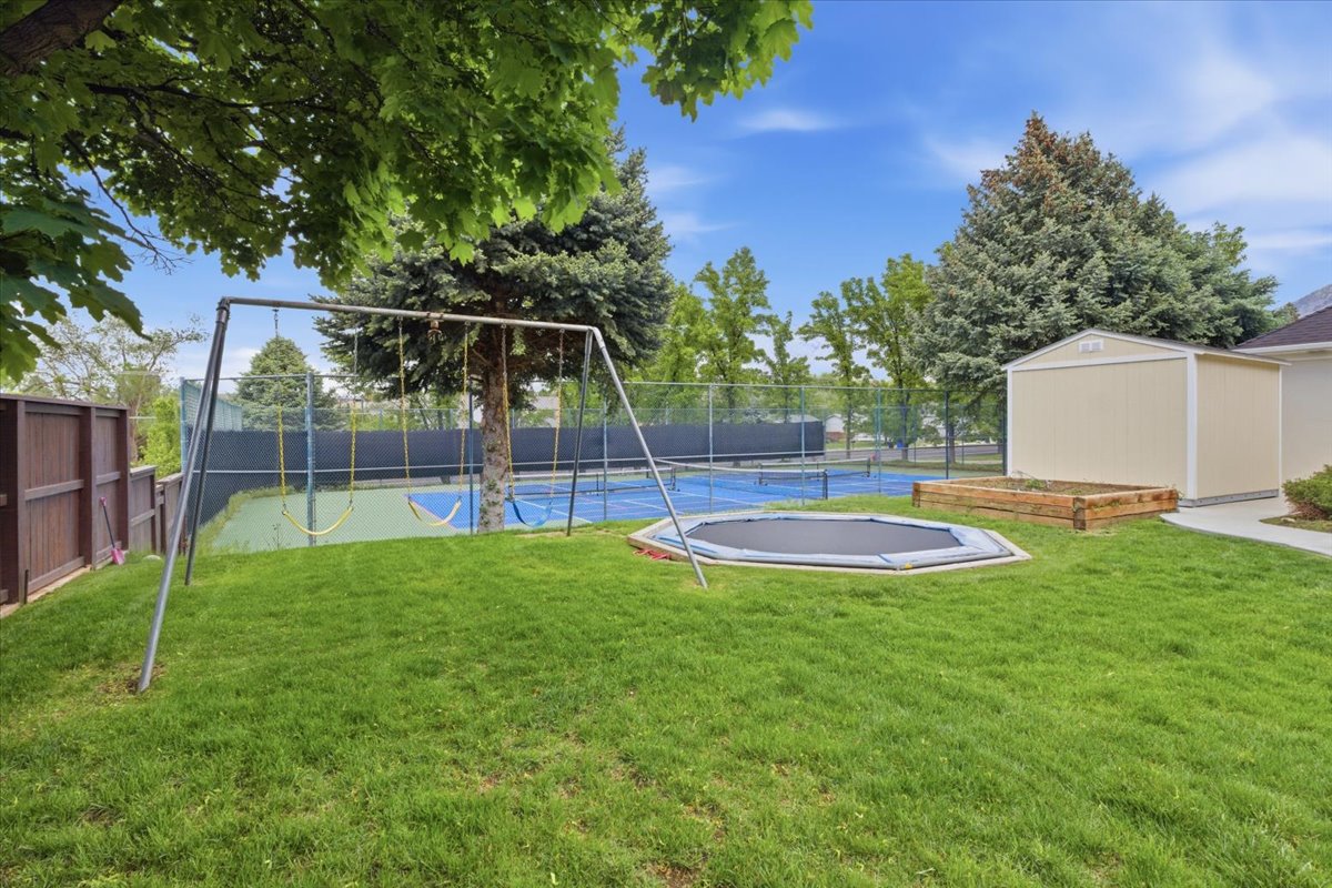 Expansive green lawn featuring a swing set, an in-ground trampoline, and a raised garden bed