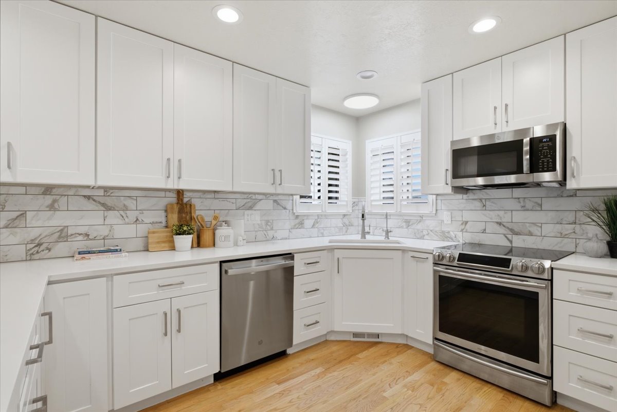 Bright kitchen featuring white shaker cabinetry, stainless steel appliances, quartz countertops, and a marbled subway tile backsplash