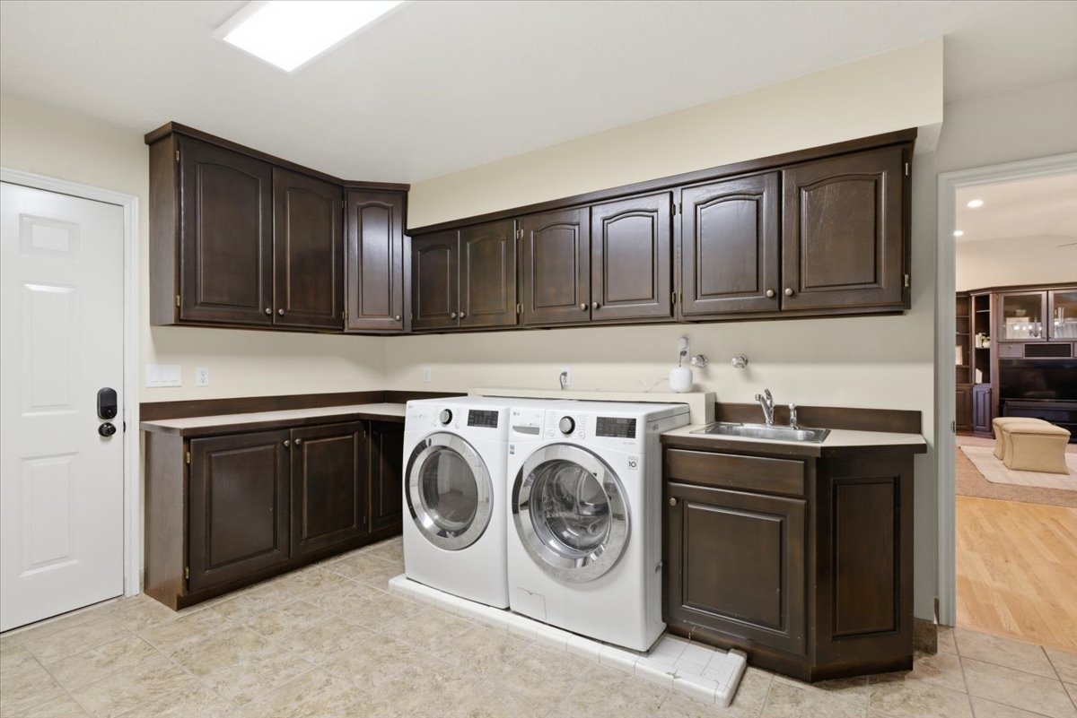 Laundry room featuring extensive dark wood cabinetry, light-toned countertops, a utility sink with a chrome faucet, and tile flooring