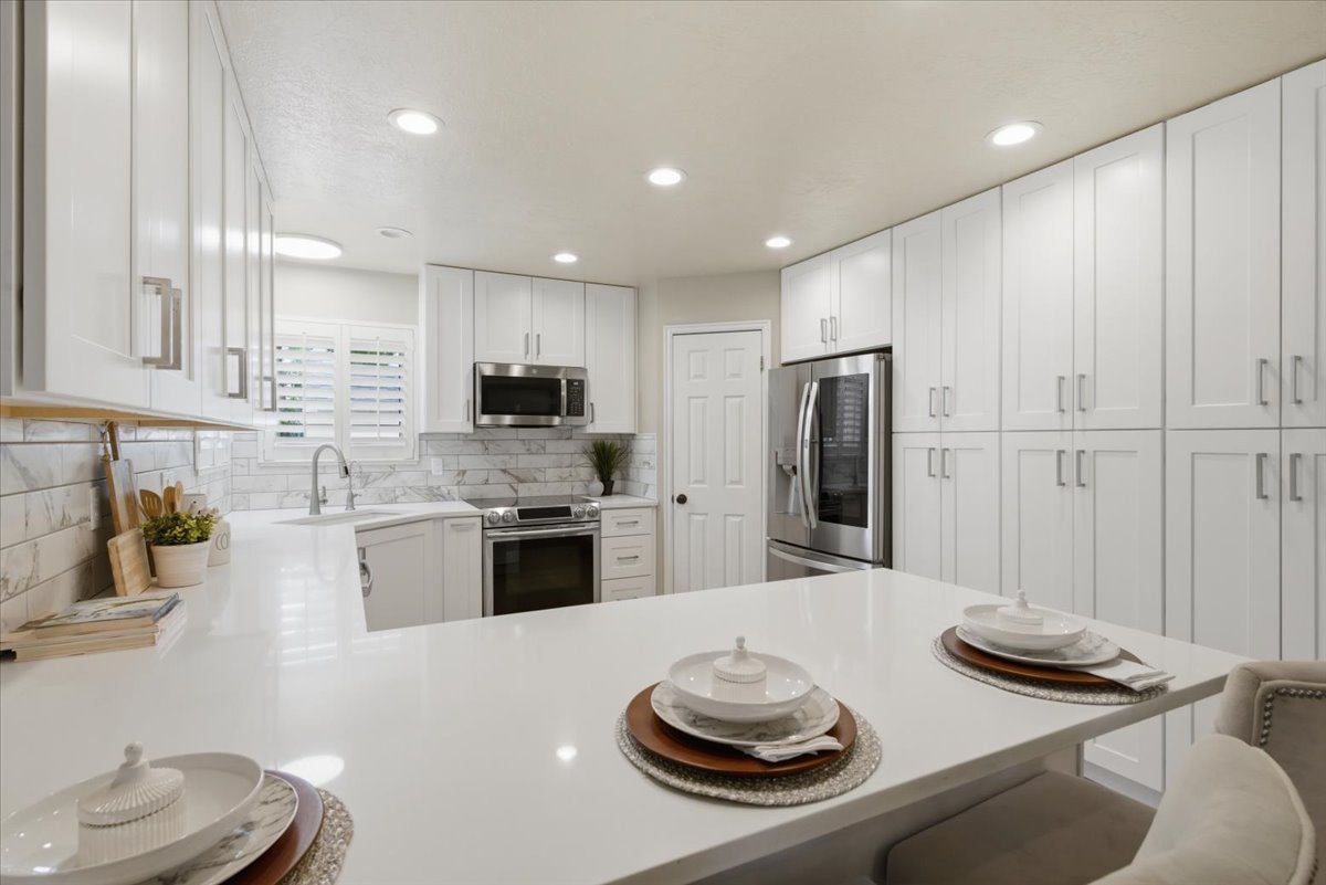 Modern kitchen featuring extensive white cabinetry, stainless steel appliances, a white solid surface countertop, white subway tile backsplash, and recessed lighting