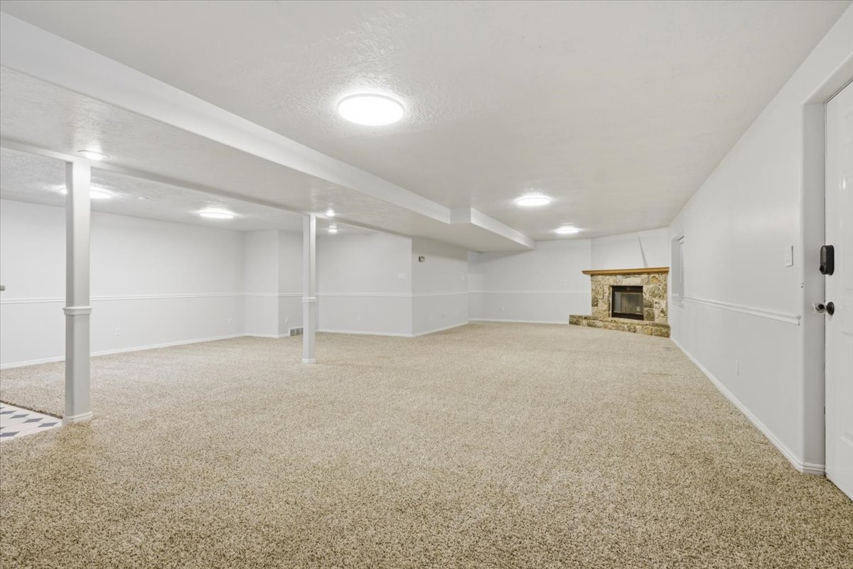 Spacious room featuring neutral carpeting, a stone fireplace with a wood-finish mantel, recessed lighting, and white baseboards