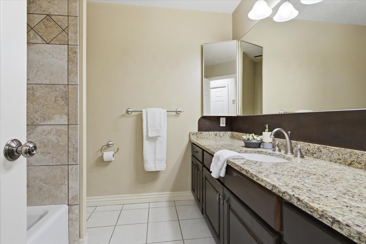 Bathroom featuring a light-toned tile floor, a built-in vanity with dark wood-finish cabinetry, and a light-toned speckled countertop