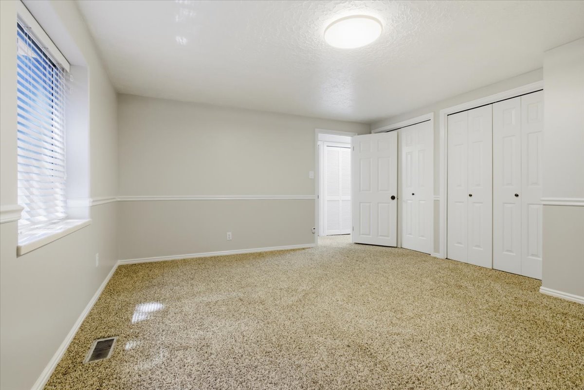 Carpeted room featuring a window with blinds, bi-fold closet doors, and a ceiling-mounted light fixture