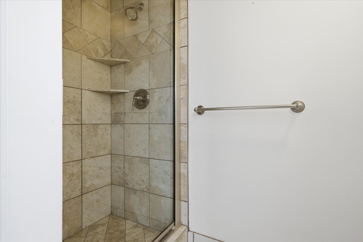 Tiled shower enclosure featuring a glass door, built-in corner shelves, and a brushed nickel shower head and control