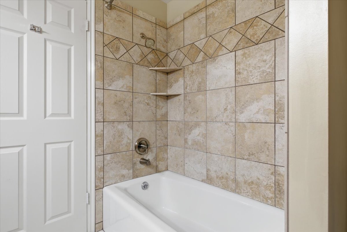 Bathtub with a tiled surround, featuring a decorative band and corner shelving