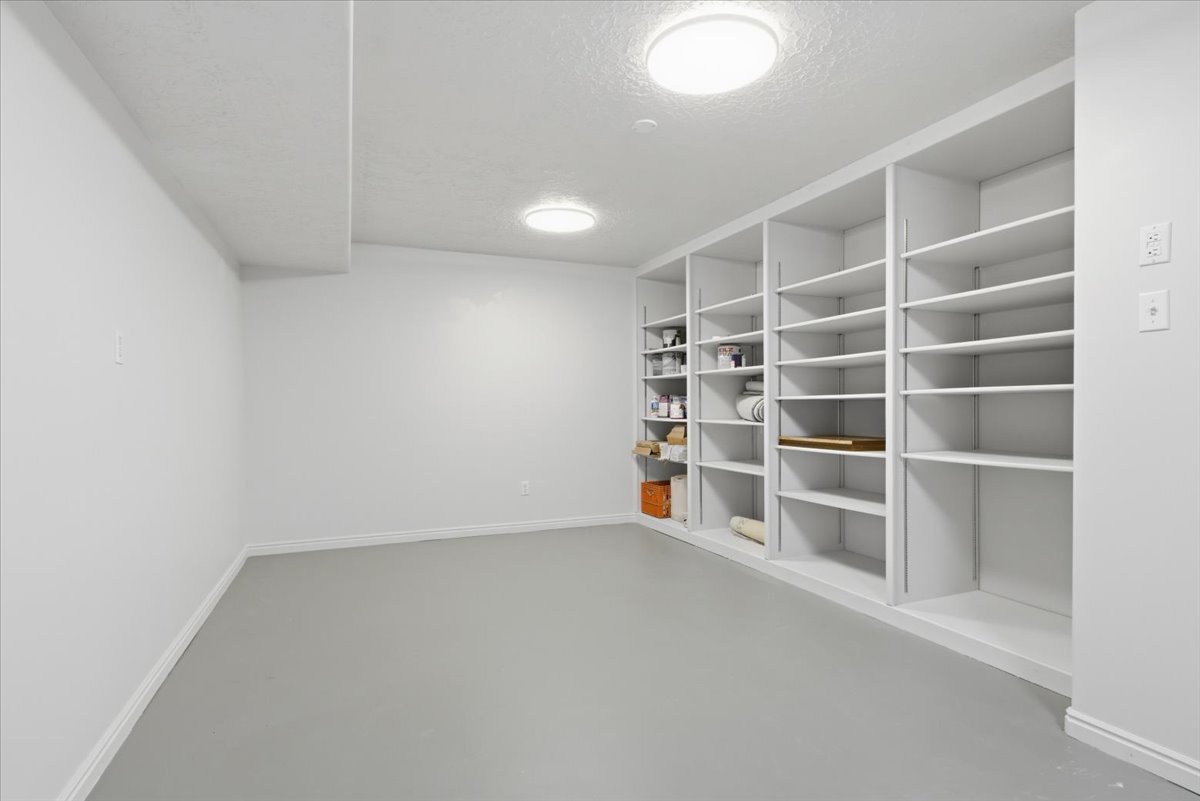Spacious utility room featuring extensive built-in shelving, durable gray flooring, and recessed ceiling lighting