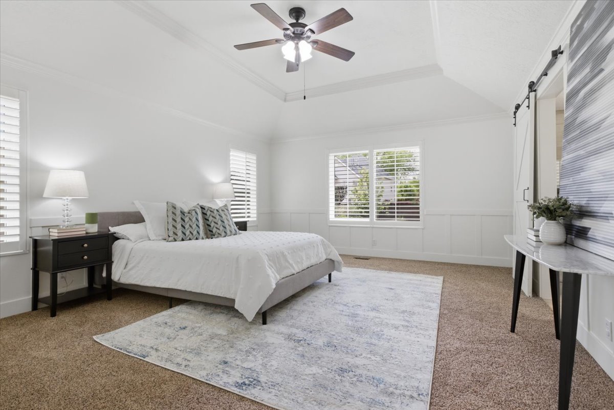 Spacious room featuring a vaulted ceiling with a ceiling fan, dual windows with plantation shutters, wainscoting, and a barn door
