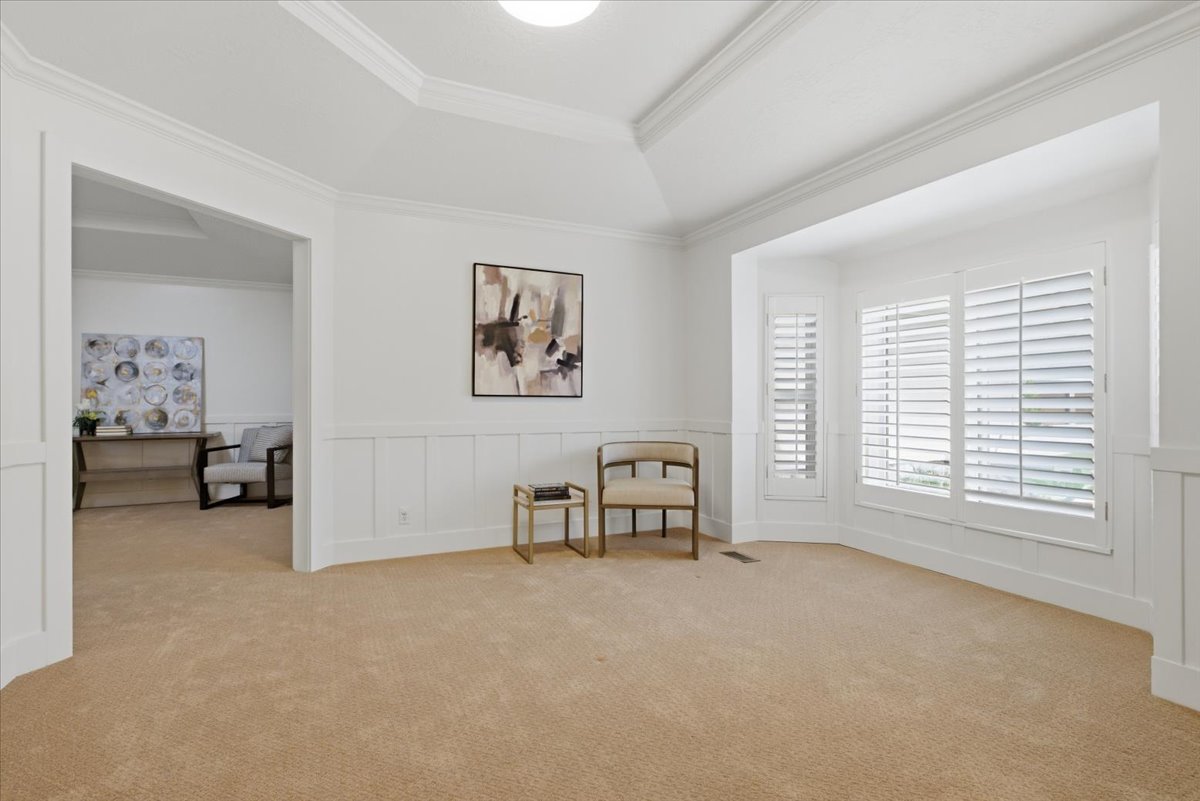 Carpeted room featuring a bay window with plantation shutters, wainscoting, crown molding, and a tray ceiling