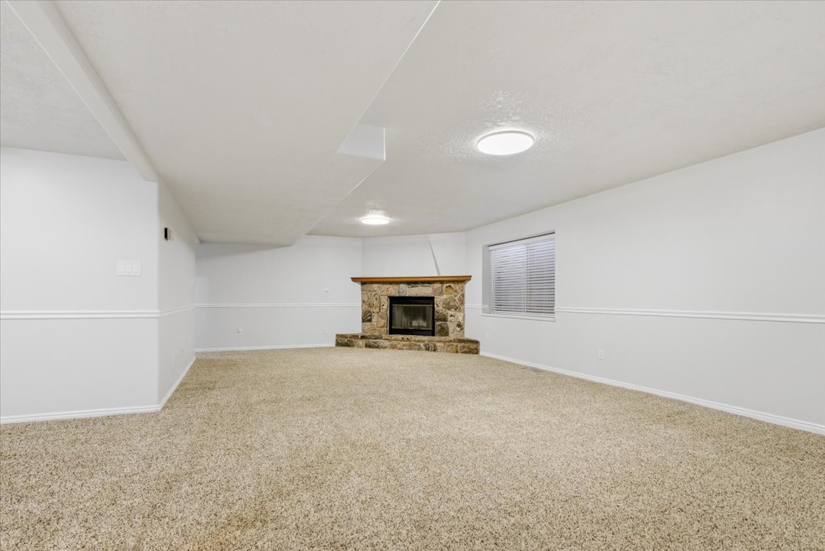 Spacious room featuring neutral carpeting, white walls with chair rail molding, and a corner stone fireplace with a wood-finish mantle