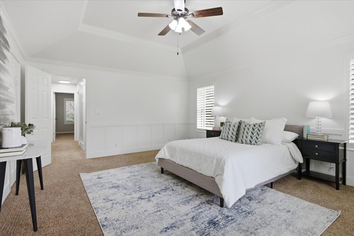 Spacious bedroom featuring a vaulted tray ceiling, crown molding, wainscoting, and wood-finish ceiling fan