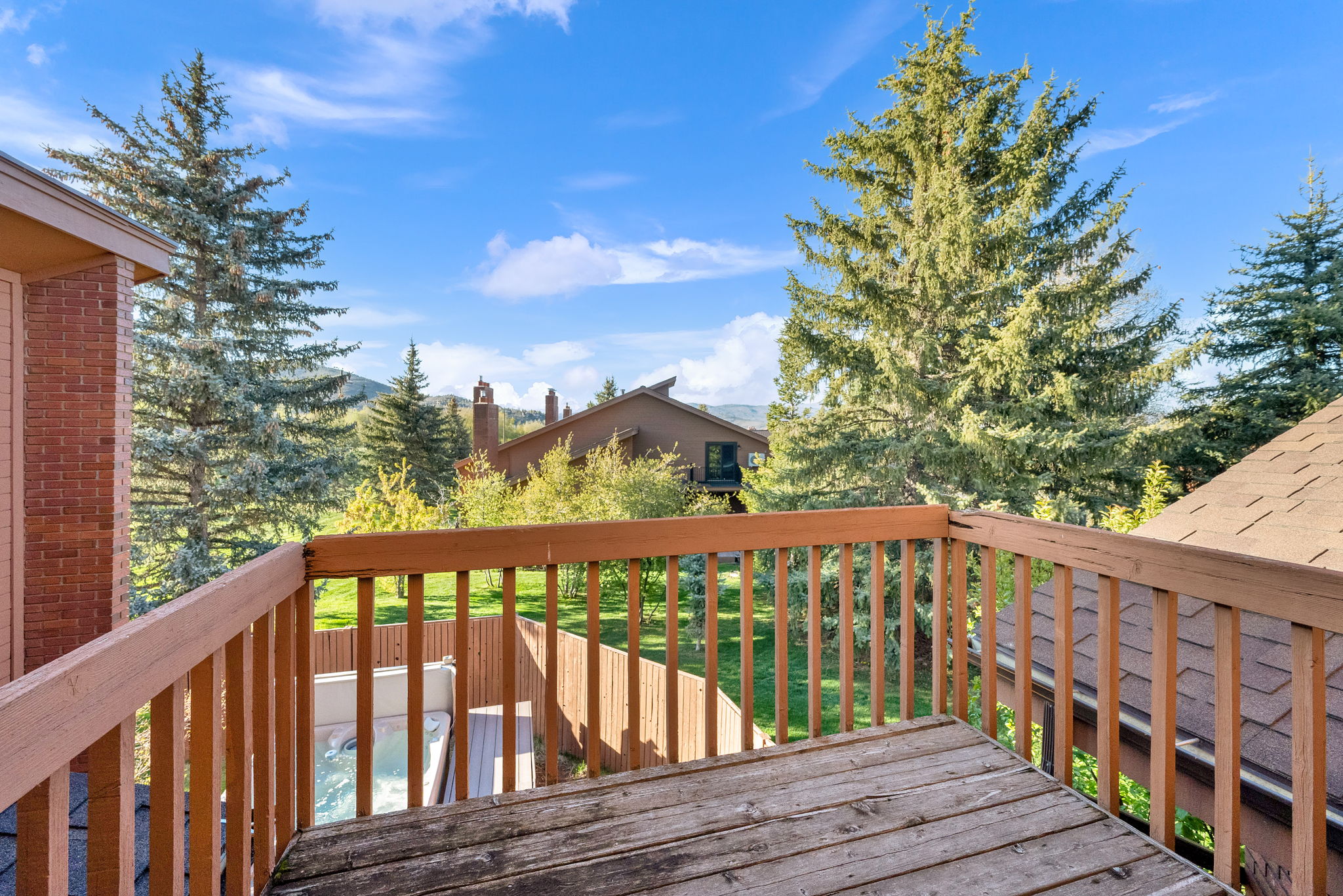 Upper-level wood deck with a slatted railing, offering expansive views of mature evergreen trees and distant mountains