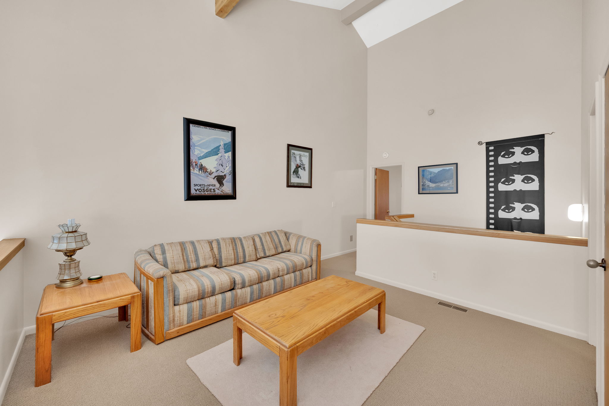 Vaulted ceiling with exposed beam, neutral wall paint, and light-colored carpeting