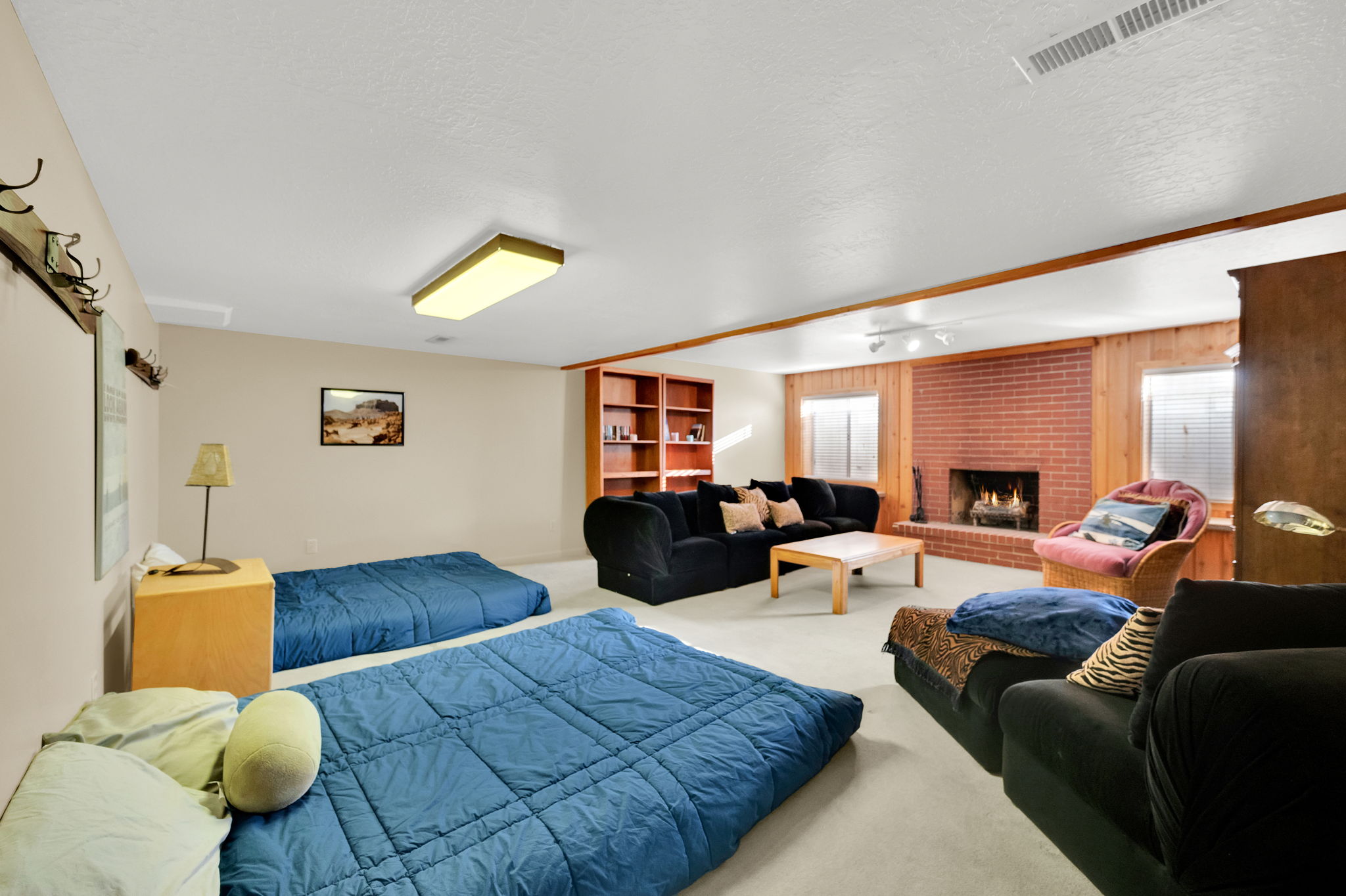 Spacious room featuring a brick fireplace, built-in shelving, wood paneling, and light-colored carpeting