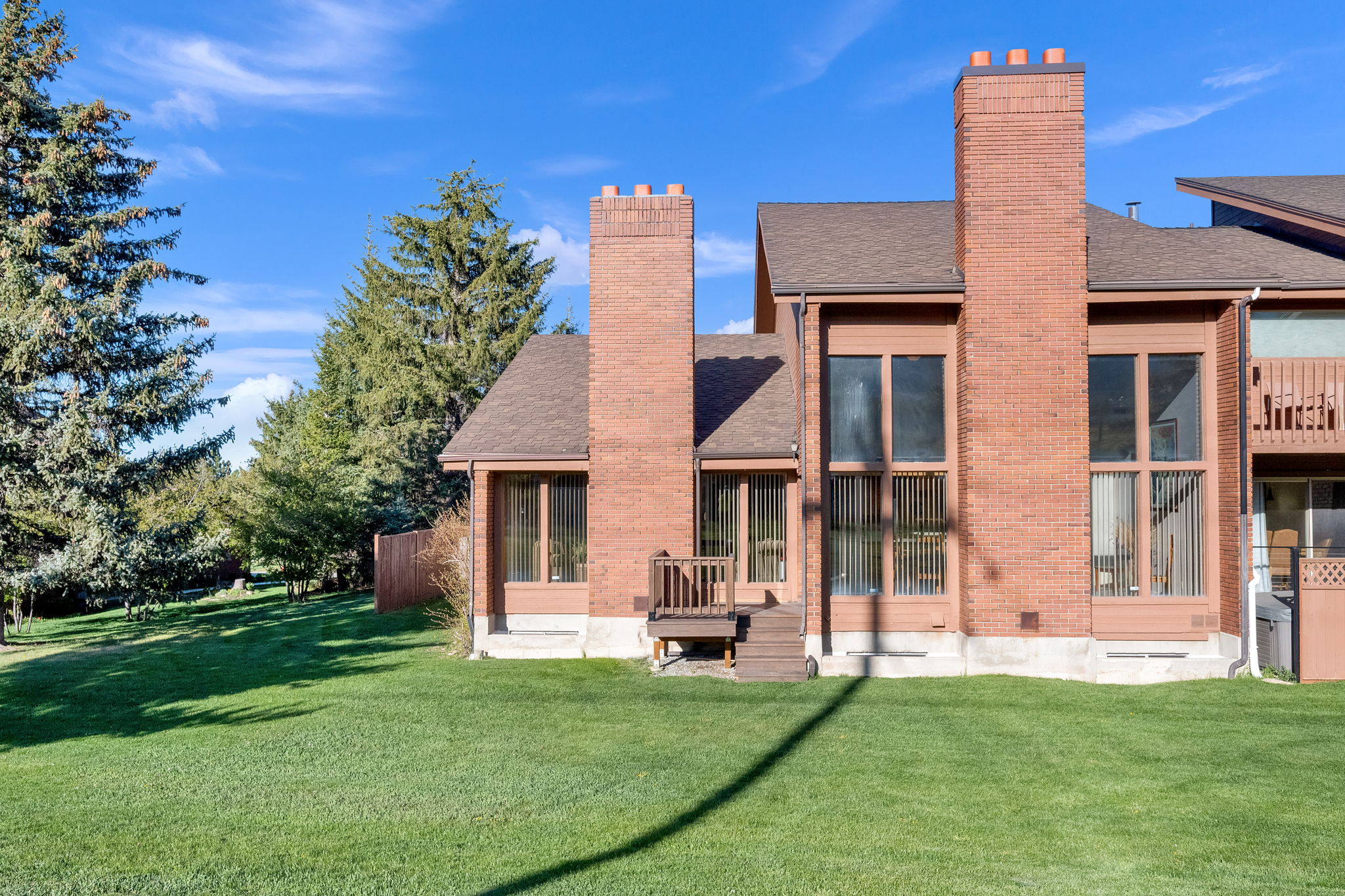 Expansive rear yard featuring a large grass area, mature evergreen trees, and a wooden fence