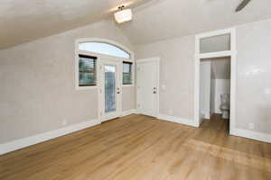 Vaulted ceiling room with wood-finish flooring, a white glass-paneled door, and an arched transom window