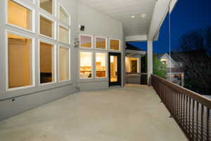Expansive concrete patio with a covered ceiling, featuring a partial railing, multiple windows offering interior glimpses, and a prominent glass-paneled door