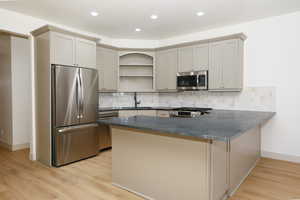 Kitchen featuring a central island with a dark countertop, light-toned cabinetry, stainless steel appliances, a tile backsplash, and wood-finish flooring