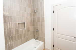 Bathtub with floor-to-ceiling vertical tile surround, integrated shower niche, chrome shower head, and chrome tub faucet