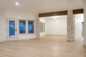 Spacious living area featuring light wood-finish flooring, recessed lighting, and a prominent stone-clad column supporting a wood beam