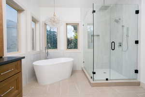 Contemporary bathroom featuring a freestanding soaking tub with a floor-mounted faucet, a glass-enclosed shower with black hardware, and light-toned tile flooring