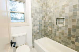 Bathroom featuring a white bathtub, tiled shower surround with an integrated niche, a white toilet, and a window with white trim