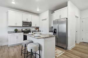 Contemporary open-concept kitchen featuring white shaker cabinetry, Gas stove, stainless steel appliances, a center island, granite countertops