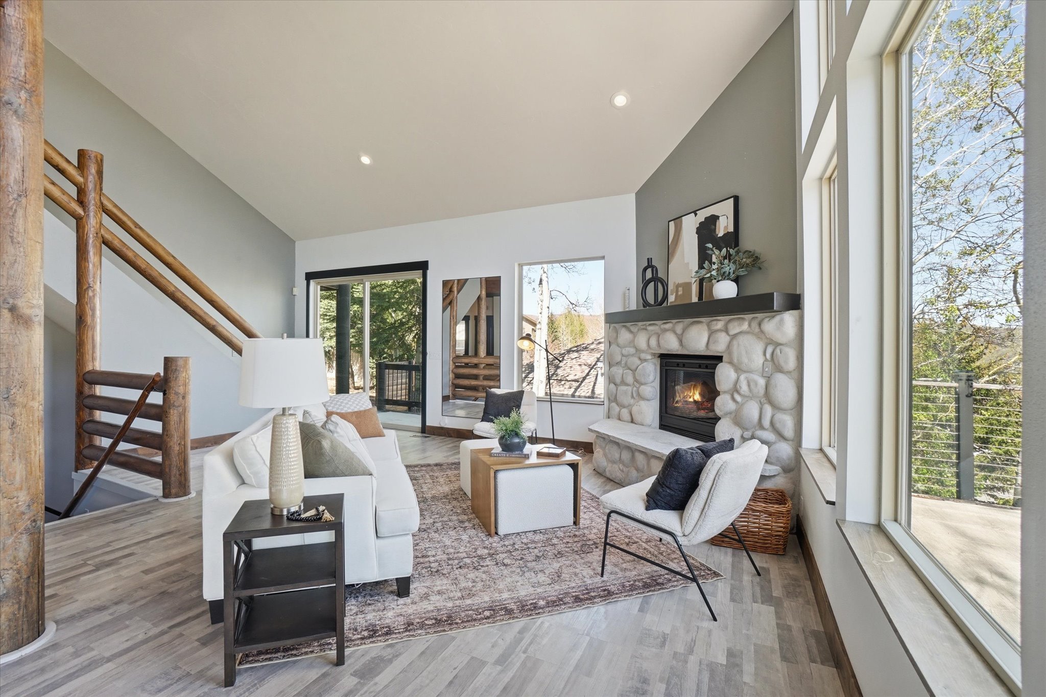 Vaulted living room featuring a stone fireplace with a hearth, and expansive windows.
