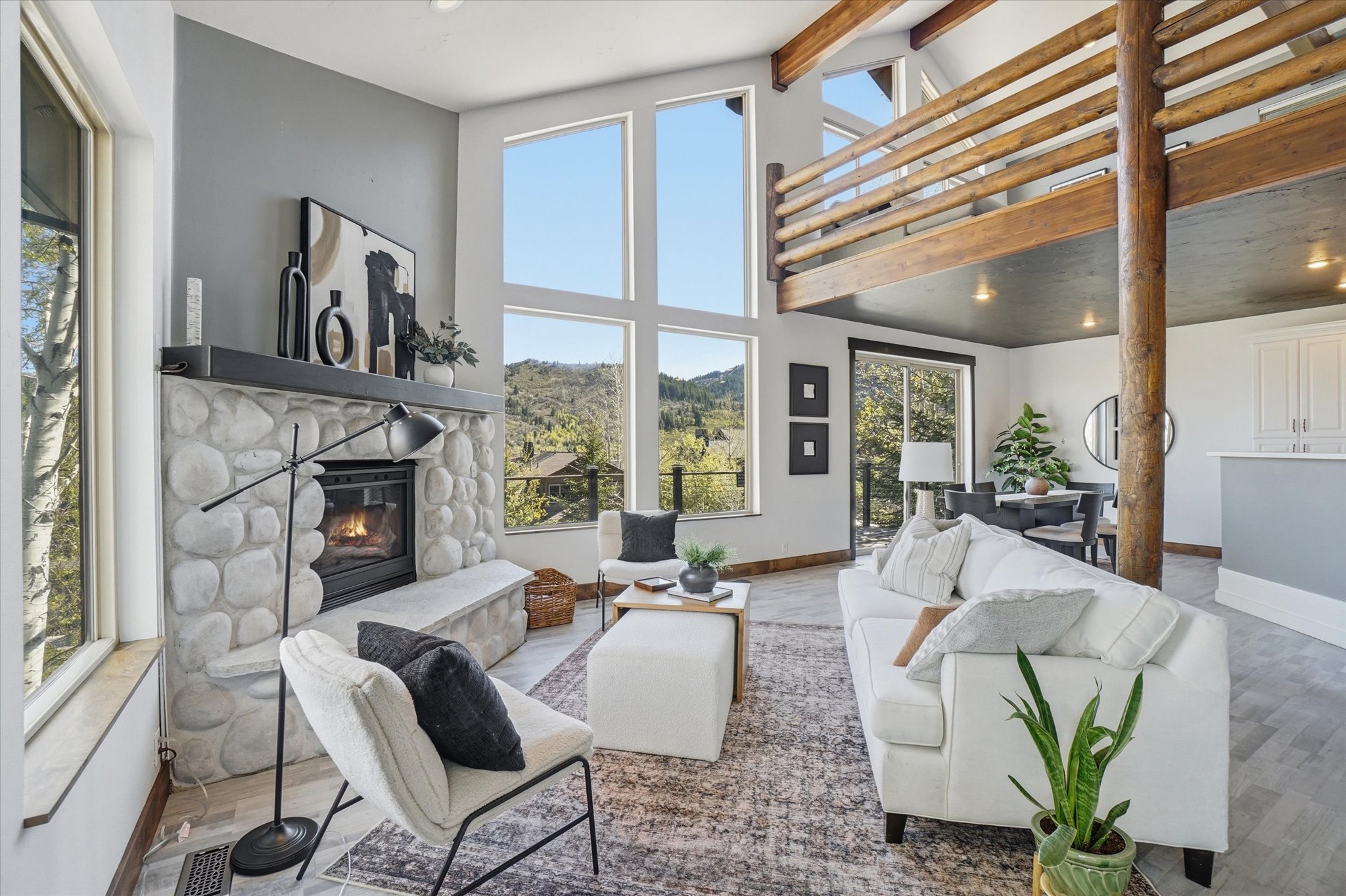 Vaulted living room featuring a stone fireplace with a hearth, and expansive windows.