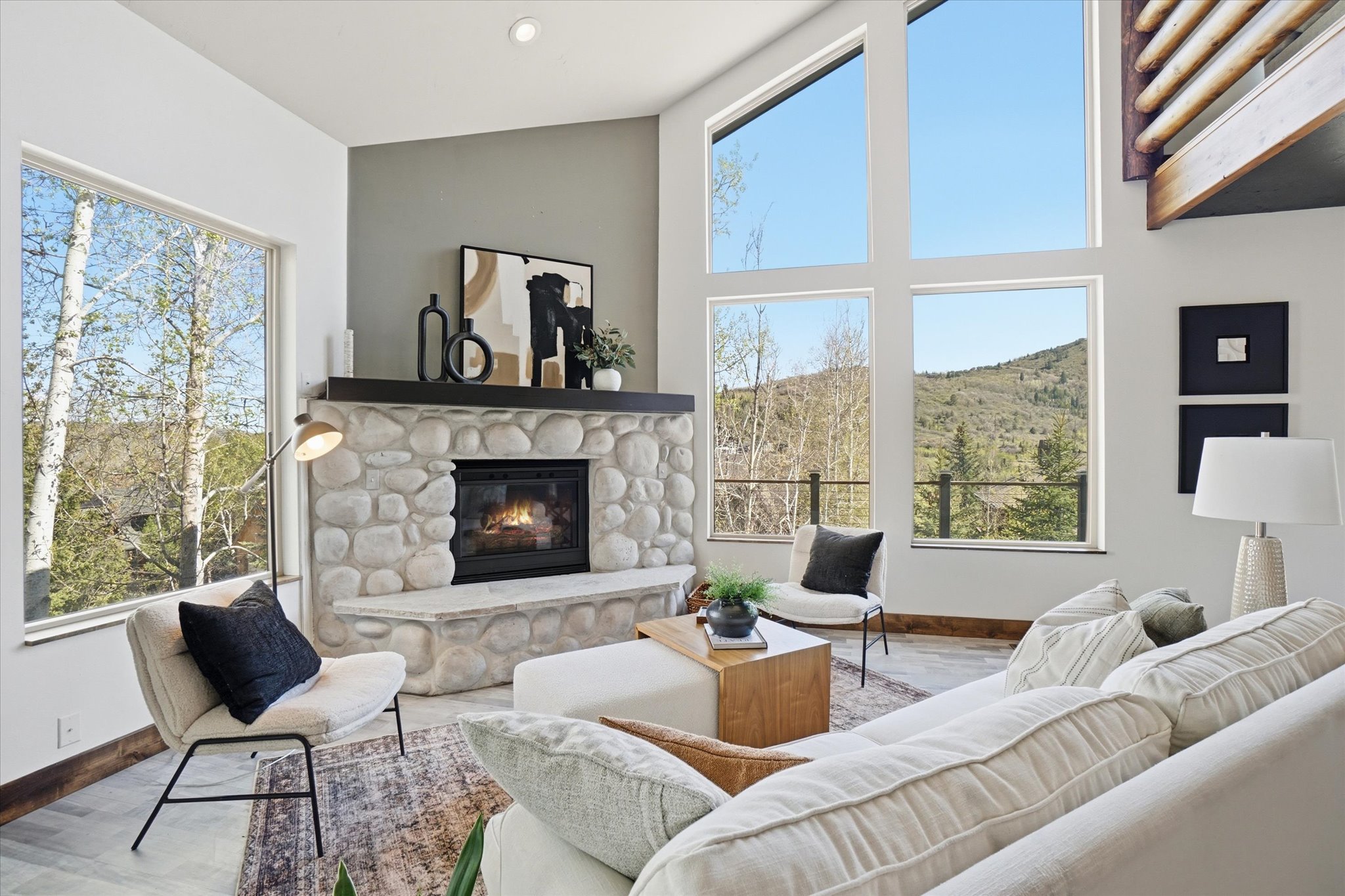 Vaulted living room featuring a stone fireplace with a hearth, and expansive windows.