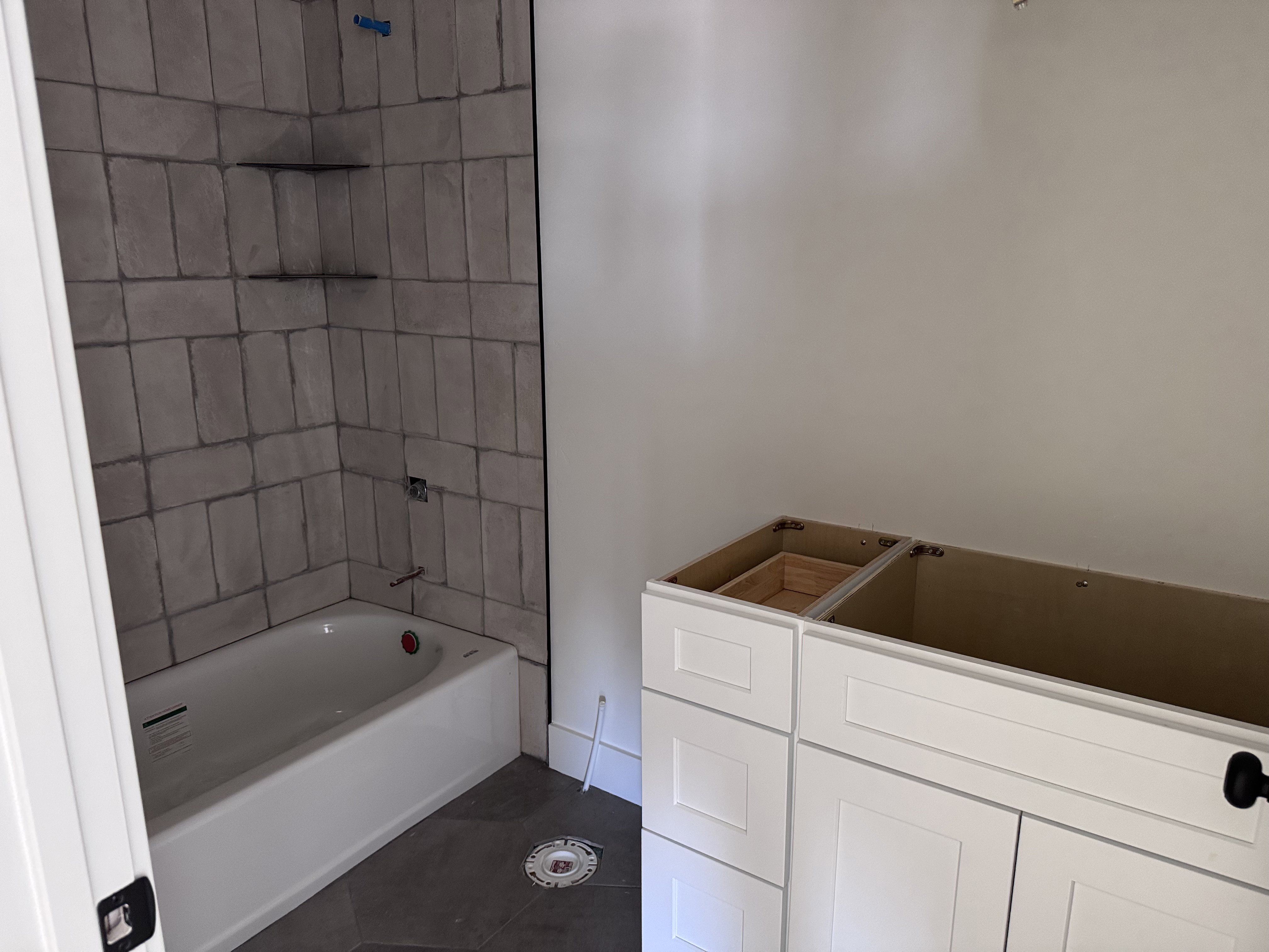 Bathroom featuring a white bathtub with tile surround, corner shelving, and a vanity base cabinet with matte black hardware