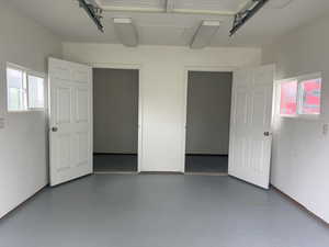 Garage interior featuring a gray epoxy floor finish, two paneled doors, two rectangular windows, and overhead fluorescent lighting fixtures