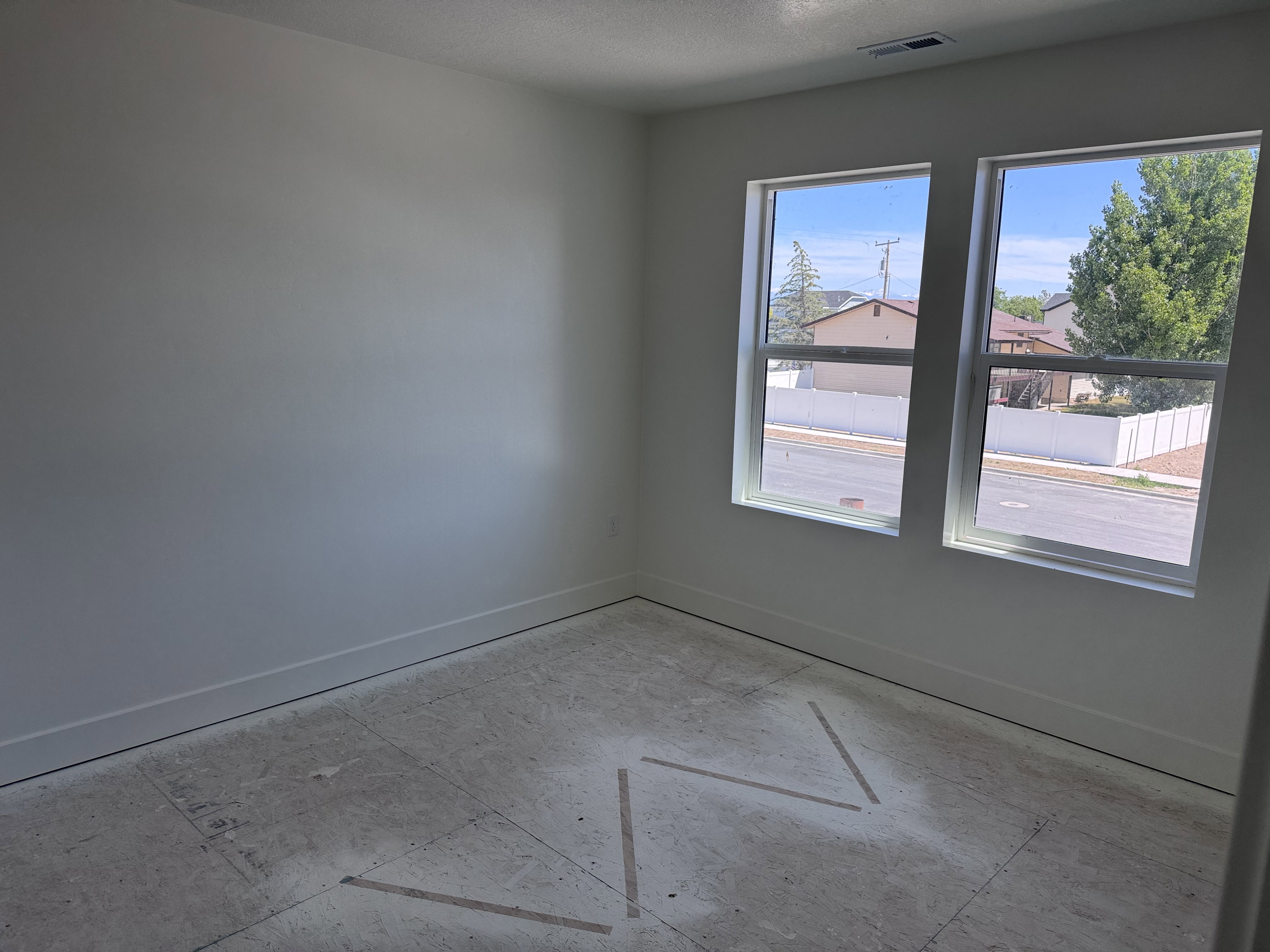 Bright interior space featuring two large windows, white walls, and a subfloor ready for finish